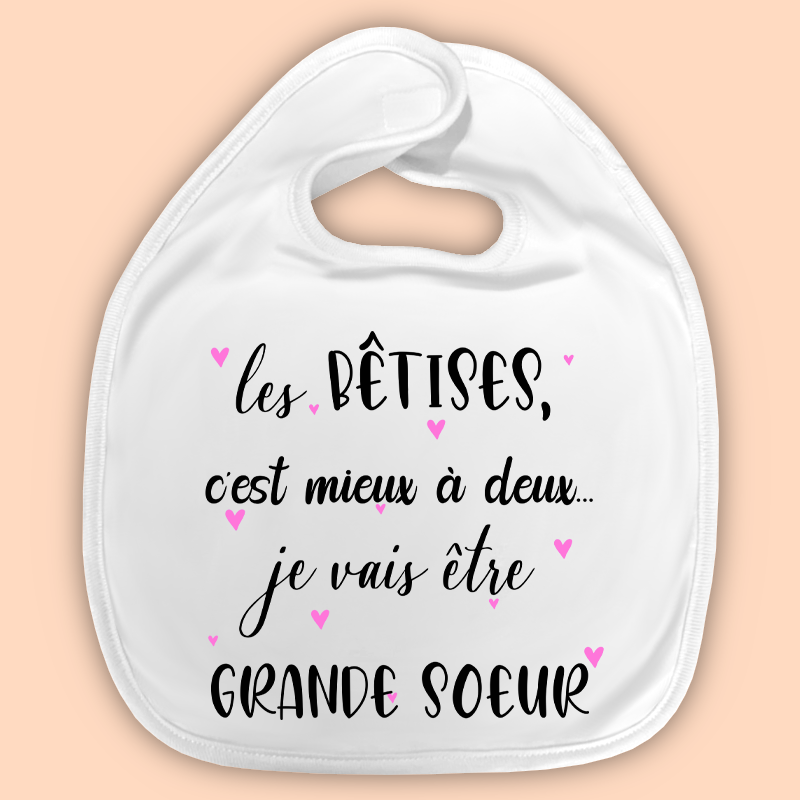 Bavoir blanc avec texte amoureux : « les bêtises, c’est mieux à deux… je vais être GRANDE SOEUR » et petits cœurs roses.