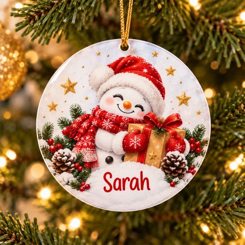 Une boule de Noël plate suspendue au sapin représente un bonhomme de neige tenant un cadeau.