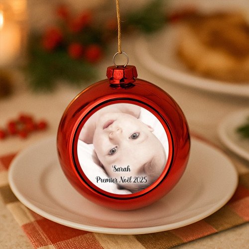 Une boule de Noël rouge personnalisée avec la photo d’un bébé est suspendue au-dessus d’une assiette.