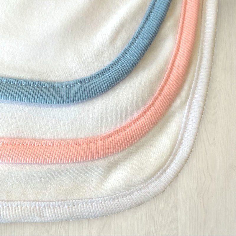 Gros plan sur des bavoirs ou cols en coton blanc avec bordures bleu pastel, rose et blanc.